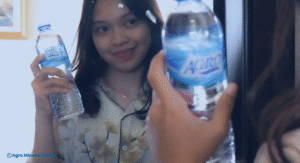 Perempuan tersenyum sambil memegang botol Agro Mineral Water di depan cermin, menggambarkan kebiasaan minum air mineral berkualitas sebagai bagian dari rutinitas sehat harian.