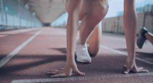 Seorang pelari dalam posisi start di lintasan lari dengan sepatu olahraga putih, siap memulai lomba.