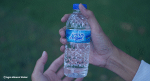 Memegang Air Mineral Dalam Kemasan Agro Mineral Water Ukuran 330ml di Lapangan 