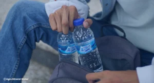 Seseorang mengambil botol Agro Mineral Water dari tas, pentingnya air minum bersih untuk mencegah gejala cacingan dan menjaga kesehatan tubuh.