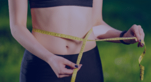 Seorang wanita mengukur lingkar pinggang dengan pita ukur kuning sebagai bagian dari cara menghitung berat badan ideal.